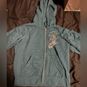 Teal Nike zip-up hoodie with stacked logos, kangaroo pockets, adjustable hood.